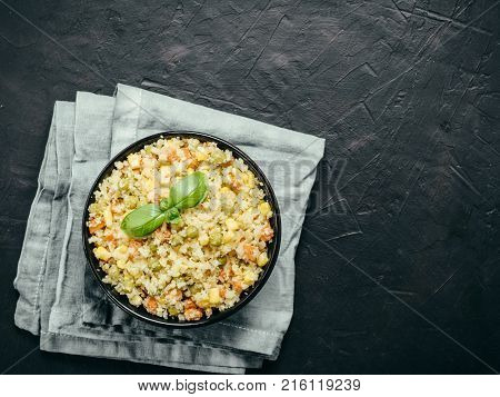 Top view of cauliflower rice with vegetables. Organic paleo Cauliflower Rice with corn, green peas and carrots on black concrete background. Copy space.