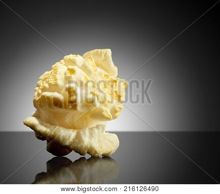 Single popped popcorn on a black background with reflection. Close-up or macro.