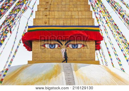 The worker strolls by the top part of a stupa of Bouda directly between closely watching Buddha's eyes. Boudnath Kathmandu Nepal on March 5 2017.
