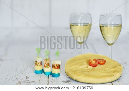 Two glasses of white wine, polenta with cherry tomato and chese canapes on a wooden background