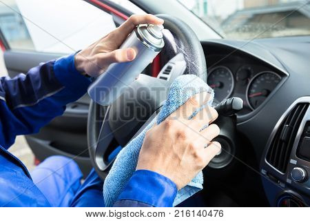 Close-up Of Worker's Hand Cleaning Car Steering Wheel Using Spray Can And Cloth