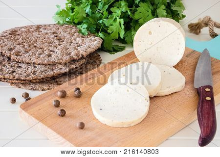 Dietary homemade boiled sausage mortadella from chicken breast with spices on a wooden cutting board. Protein rye multicereal flatbread. White background.