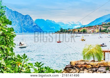 Amazing landscape of shore of Brenzone commune city Lake Garda with mountains cloudy sky and ships in northern Italy. Veneto region