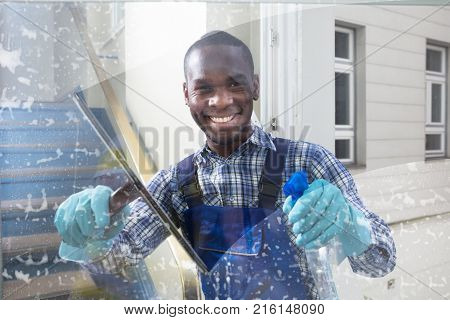 Happy Male Worker Cleaning Glass With Squeegee And Spray Bottle