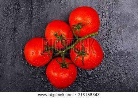 Ripe, juicy, appetizing, bright tomatoes on a green branch, lie on a black background.