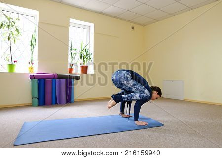 Sportswoman focused on stretch before Pilates class. Girl doing warm up for legs on mat. Female has hair pulled back, concentrated look. Athlete dressed in dark top, yoga legging trains in fitness room. Concept of online training, customizable workouts.