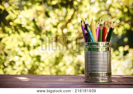 Iron bank with colored pencils on a wooden table. Eco-style. Copy space