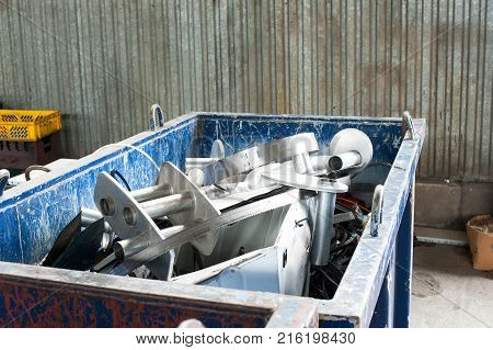 Waster metallic container bin with full with rubbish on factory in workshop. Horizontal colored image.