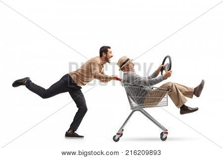 Young man pushing a shopping cart with a mature man riding inside it and holding a steering wheel isolated on white background