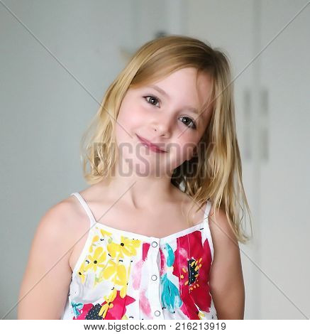 A cute six year old blonde girl in a summer white dress with flowers smiling on an abstract background
