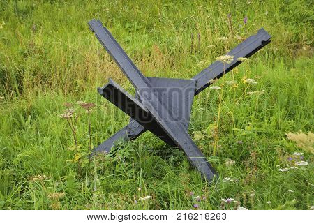 A black antitank hedgehog of the war stands on the green grass. The concept of war and peace.
