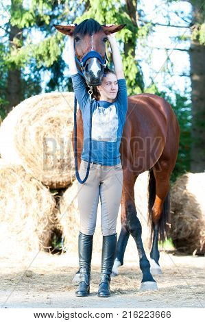 Young cheerful teenage lady equestrian have fun with her favorite chestnut horse at ranch. Vibrant colored outdoors vertical summertime image.