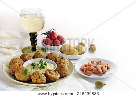 appetizers and a glass of white wine spanish tapas such as baked olives prawn shrimps potatoes tomato and garlic sauce as a corner background on white with copy space selective focus