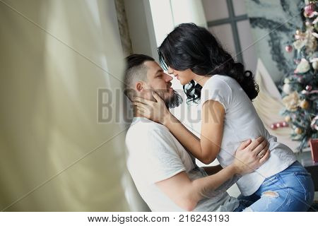 Beautiful young couple in love decorating Christmas tree, arranging the christmas lights and having fun