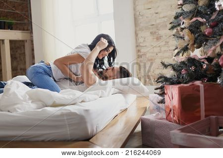 Beautiful young couple in love decorating Christmas tree, arranging the christmas lights and having fun