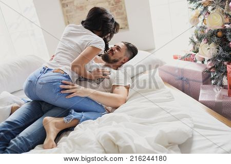 Beautiful young couple in love decorating Christmas tree, arranging the christmas lights and having fun