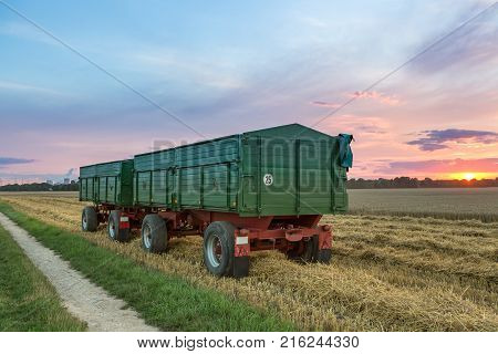 Green Agriculture trailer covered with a tarp, loaded with harvest. At sunset