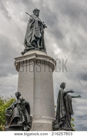 Adelaide SA Australia - November 20 2009: Monumental statue of King Edward VII in full coronation regalia under heavy cloudscape on pedestal with two female statues at foot. Green foliage.