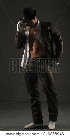 Young sexy muscular man in a suit, hat and white gloves view near black wall