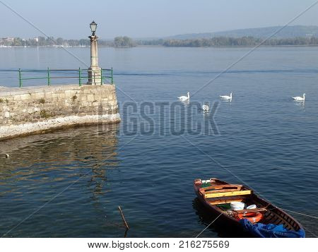 View of Lake Maggiore from the coast of Arona with streetlight pier boat and swans