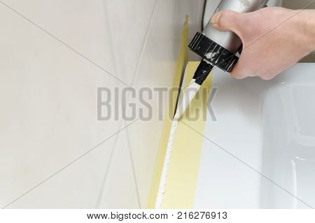 A man is puting the silicone sealant to caulk the joint between a washbasin and a wall.