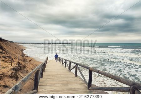 Man Walking On Boardwalk In A Stormy And Clouded Day In The Mediterranean Sea. Guardamar Del Segura 