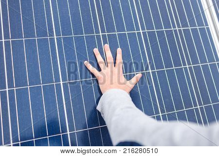 The hand of the European man lies on the panel of a modern solar battery. Outdoors.