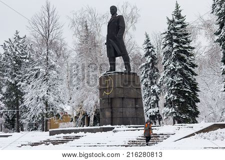 Makeevka Ukraine - November 22 2017: Woman in an orange waistcoat cleans the snow near the monument to the communist leader Lenin in a snow-capped city