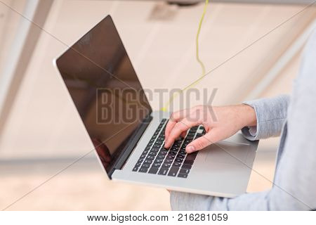 Hands of a man working on a modern laptop, connected to a solar panel.