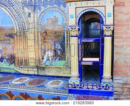 Historic Bookshelf at Spain Square (Plaza de Espana) in Seville City, Spain. Ceramic Ornamental Colorful Tile and Small Bookcase for BookCrossing. Place for Leaving and Picking Up a Free Book in City.