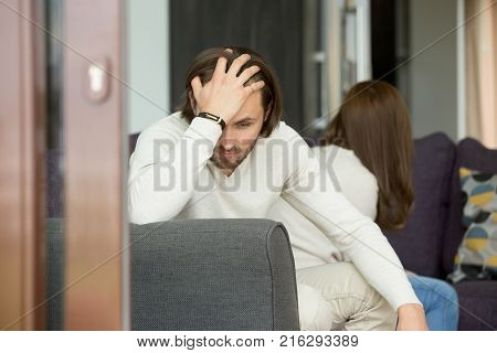 Upset man thinking of unresolved problems fed up with misunderstandings in bad relationships sitting his back to frustrated woman on sofa at home holding head in hand, unhappy couple after quarrel