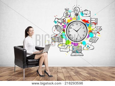 Portrait of a cheerful young woman sitting in an armchair with a laptop. A concrete wall background with a tme management sketch