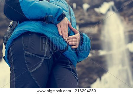 Closeup of female hands forming a hearth on her belly in nature. Motherly love outdoor.