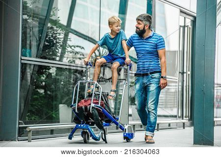 Happy father and son happy and excited together for the trip boy sitting and cheering on baggage trolley. Holiday vacation traveling abroad concept copy space
