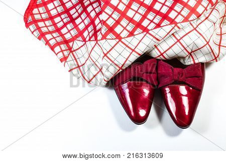 Top view of women's vintage red shoes with bows with red and white plaid scarf on white background copy space horizontal aspect