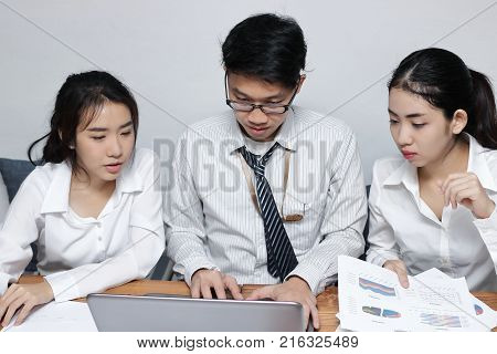 Front view of young Asian business people working together on a laptop computer at office. Teamwork brainstroming concept. Selective focus and shallow depth of field.