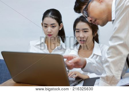 Young Asian business people working together on a laptop computer at office. Teamwork brainstroming concept. Selective focus and shallow depth of field.