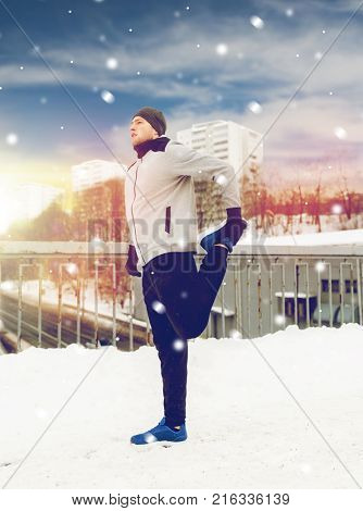fitness, sport, people, exercising and healthy lifestyle concept - young man stretching leg and warmig up on snow covered winter bridge