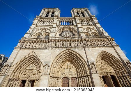 Details close up bottom view of French Gothic architecture of Notre Dame cathedral of Paris, France. Sunny blue cloudy sky. Our Lady of Paris church. Central main facade.