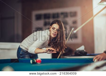 Young beautiful young woman aiming to take the snooker shot while leaning over the table in a club