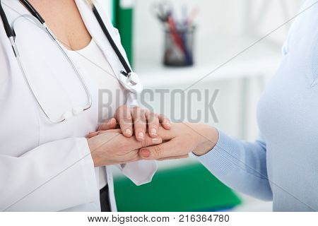 Hand of doctor reassuring her female patient. Medical ethics and trust concept