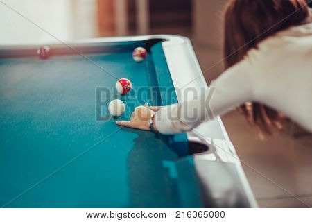 Young beautiful young woman aiming to take the snooker shot while leaning over the table in a club