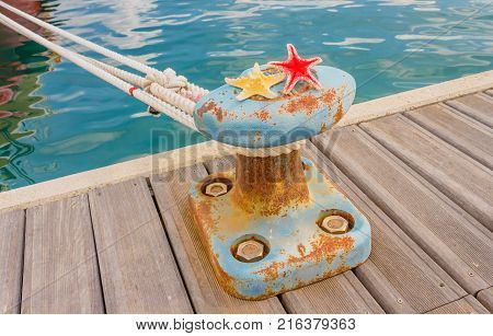 detail of a bitt with two starfishes and a rope for mooring at the harbor  /the bitt is a low cast-iron column in the shape of a mushroom to tie chains and mooring ropes