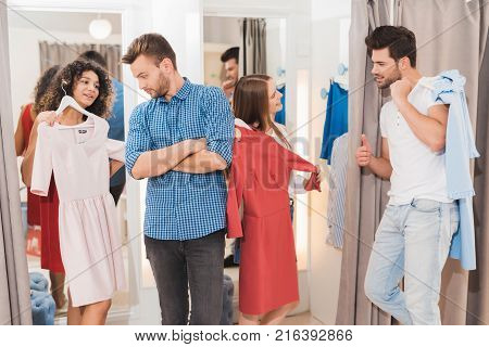 Men in the fitting room are waiting for their girls. Girls trying on things in the fitting room. Young people try on clothes in fitting room.