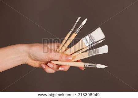 Hands holdinh brushes over dark gray background.