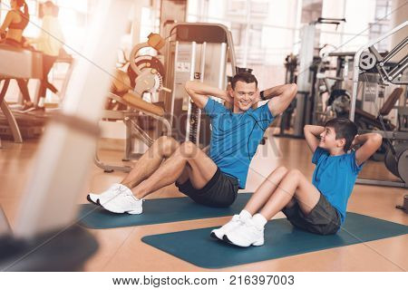 Father with his son in the same clothes in the gym. Father and son spend time together and lead a healthy lifestyle. Man and boy are pump the abdominals.
