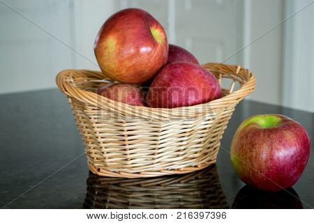A wicker basket filled with red mccoun apples on the kitchen counter with one apple beside it.