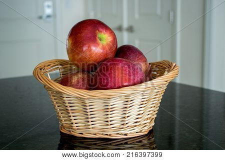 A wicker basket of red apples placed on a granite counter in the kitchen.