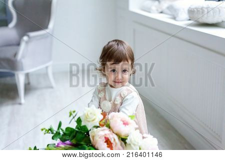 Funny and cute brunette little smiling girl with flowers in bright room