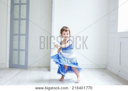 Funny and cute brunette little smiling girl playing and dancing in bright room